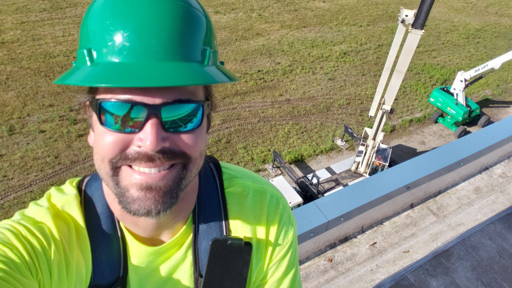 Dan wears a hardhat on a rooftop with equipment in the background.