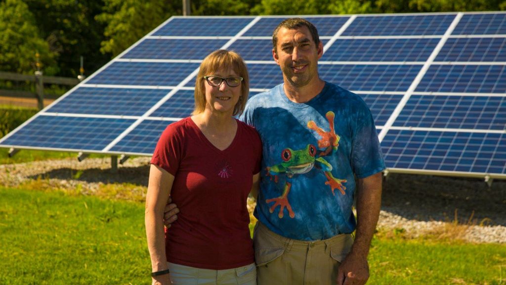 A happy couple pose for the camera in front of their ground-mount solar system. 