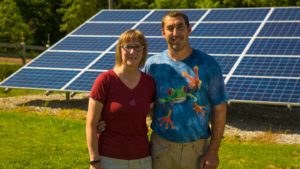 A happy couple pose for the camera in front of their ground-mount solar system.